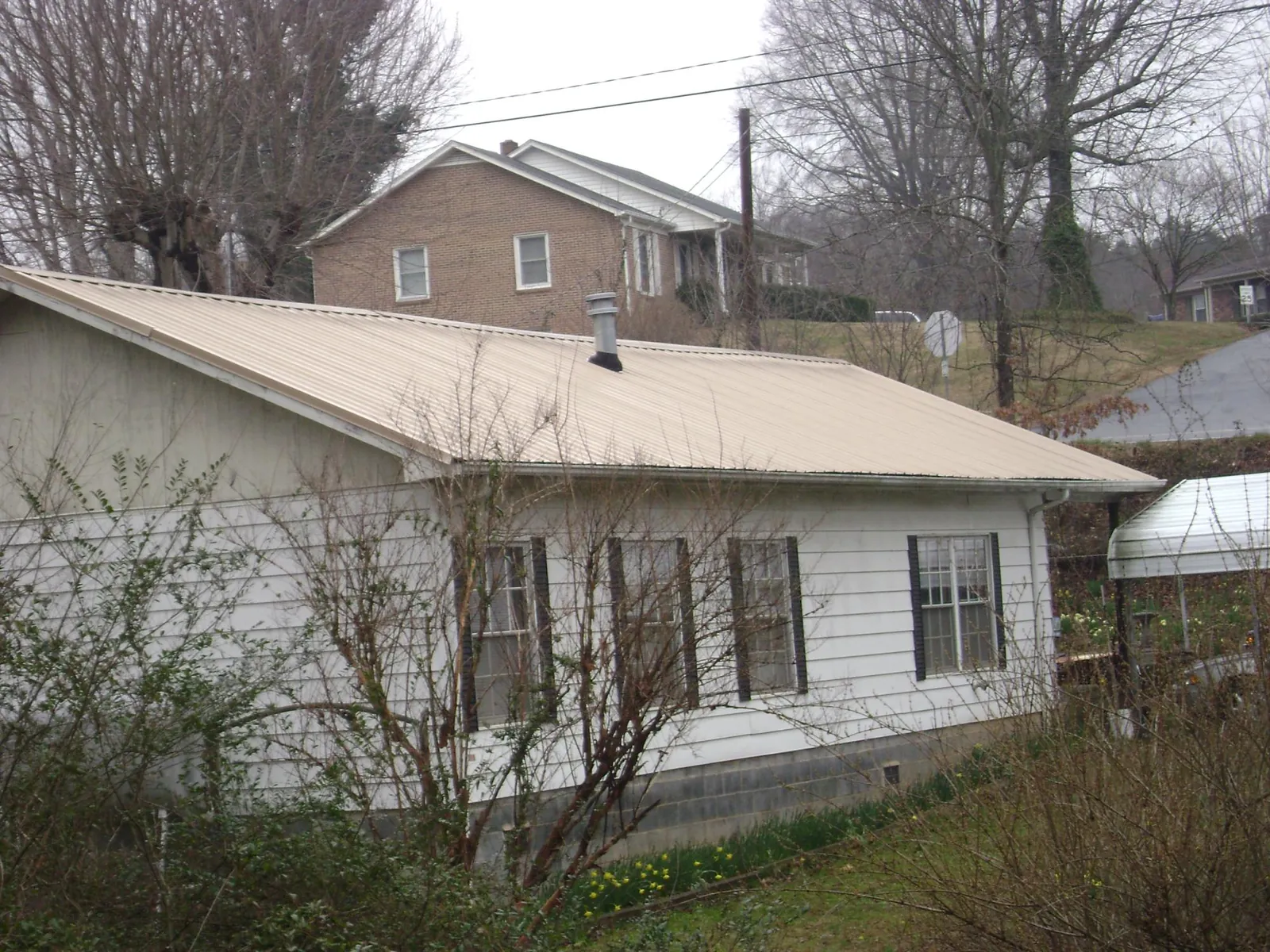 Tan metal roof on a white sided house set into a hillside — Commercial Roofing by Roofing Brothers in Upton